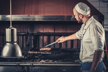 restaurant chef preparing a beef steak in a barbecue oven