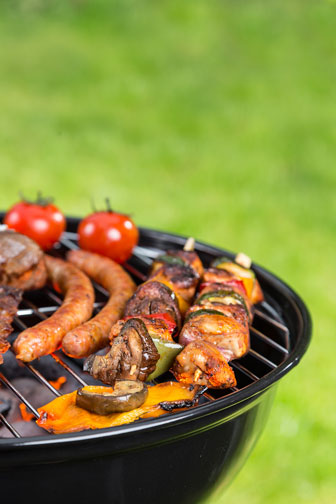 grilling various meats and tomatoes on a kettle barbecue grill